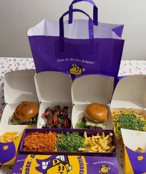 Öppnade hamburgerlådor och flatbox med mat, tillsammans med tryckt takeaway-påse